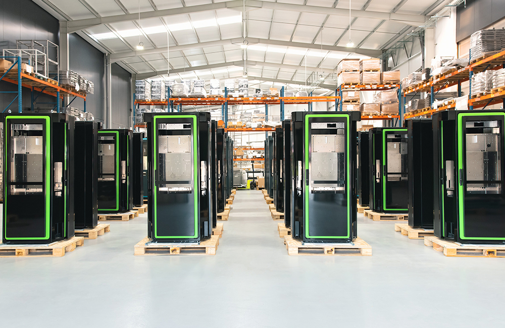 Filas de armários ou racks industriais pretos, alinhados sobre paletes numa fábrica ou armazém moderno, com prateleiras industriais e materiais armazenados ao fundo